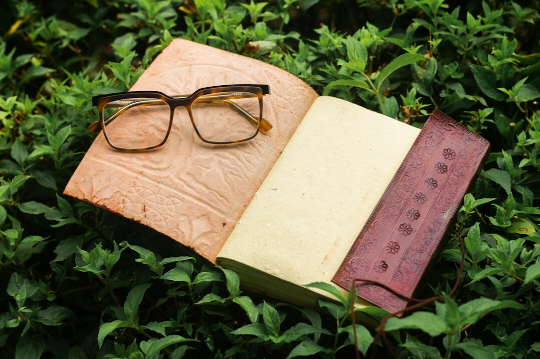 Shelf of leather-bound books stacked beside reading glasses